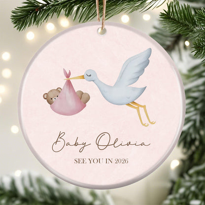 Stork and baby bear themed pregnancy announcement ornament, marked "See You in 2026". Customizable with baby’s name, soft pink design ideal for expecting parents as a holiday or milestone keepsake.