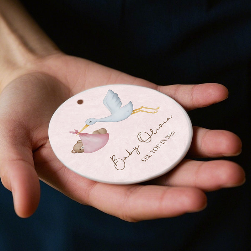 Personalized ornament with stork delivering baby bear, "See You in 2026" message. Soft pink design, perfect pregnancy announcement or baby milestone gift for new parents-to-be.