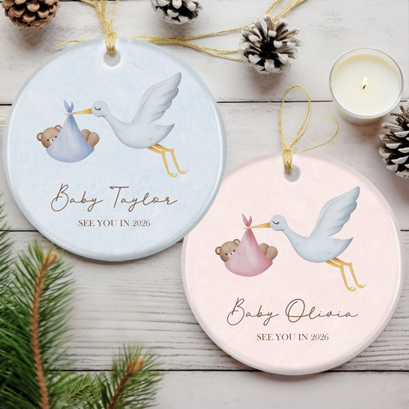 Custom ornament featuring stork delivering baby bear, "See You in 2026" message. Soft pink design, ideal for expecting parents as a personalized pregnancy announcement or holiday keepsake.